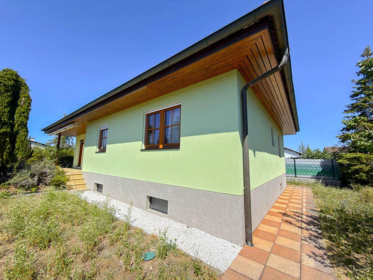 Seitenansicht des Hauses mit hellgrüner Fassade und Holzdachüberstand.