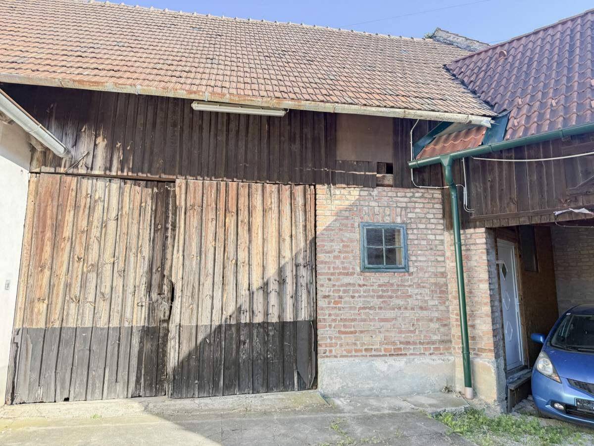 Große Holztore einer Scheune mit Ziegelmauerwerk und einem blauen Auto im Eingangsbereich.