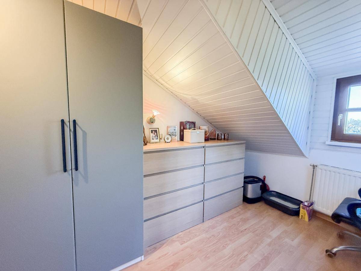 Dachgeschoss-Schlafzimmer mit schräger Decke, Holzpaneelen und integrierten Schränken.