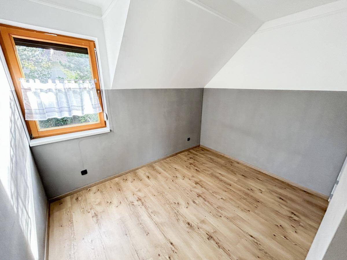 Kleines Zimmer mit Dachschräge, Holzboden und Fenster.