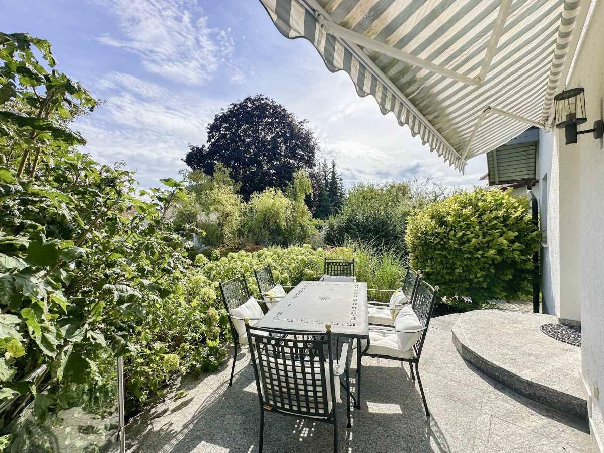 Sonniger Terrassenbereich mit Esstisch, Markise und Blick in den grünen Garten.