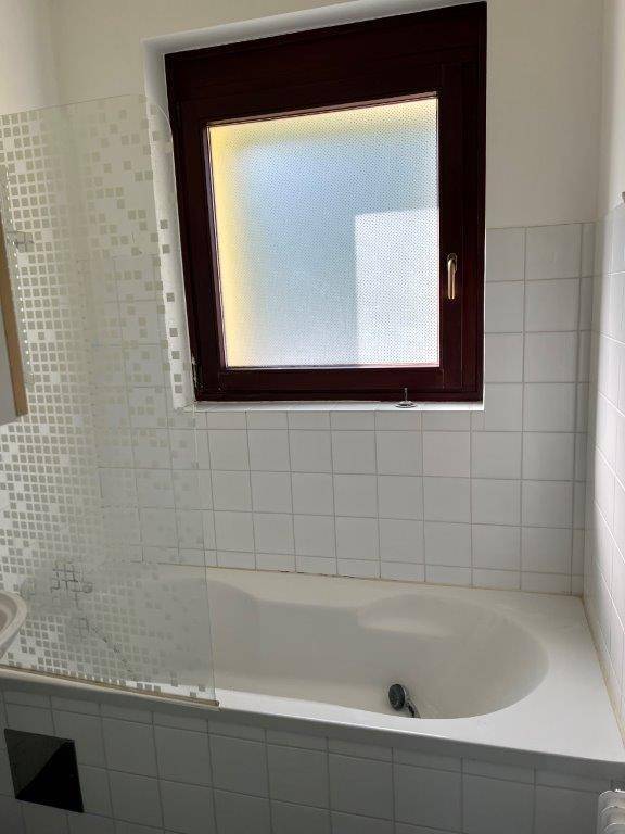 Badezimmer mit Badewanne, weißen Fliesen und einem Fenster für natürliche Belüftung.