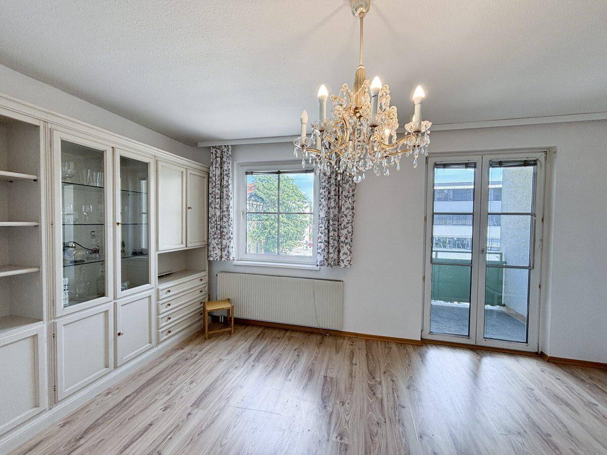 Helles Wohnzimmer mit Laminatboden, Kronleuchter und Blick ins Grüne vom Fenster.