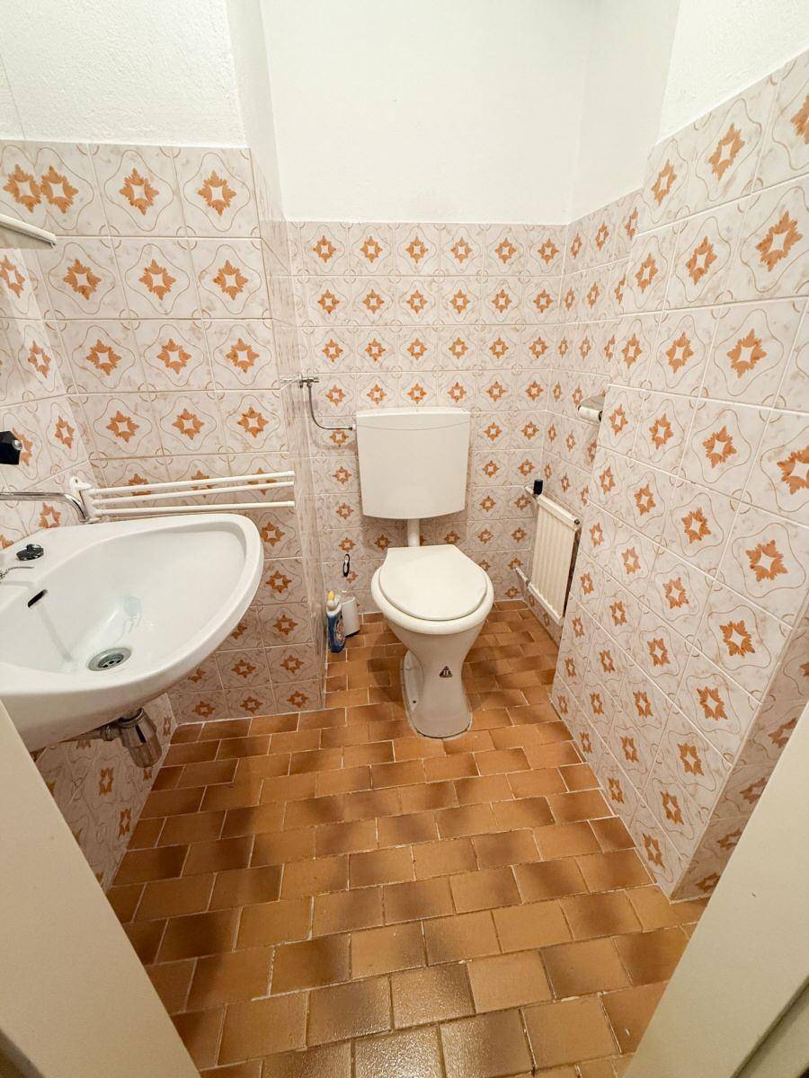 Kleines Badezimmer mit orange-gemusterten Fliesen und WC.
