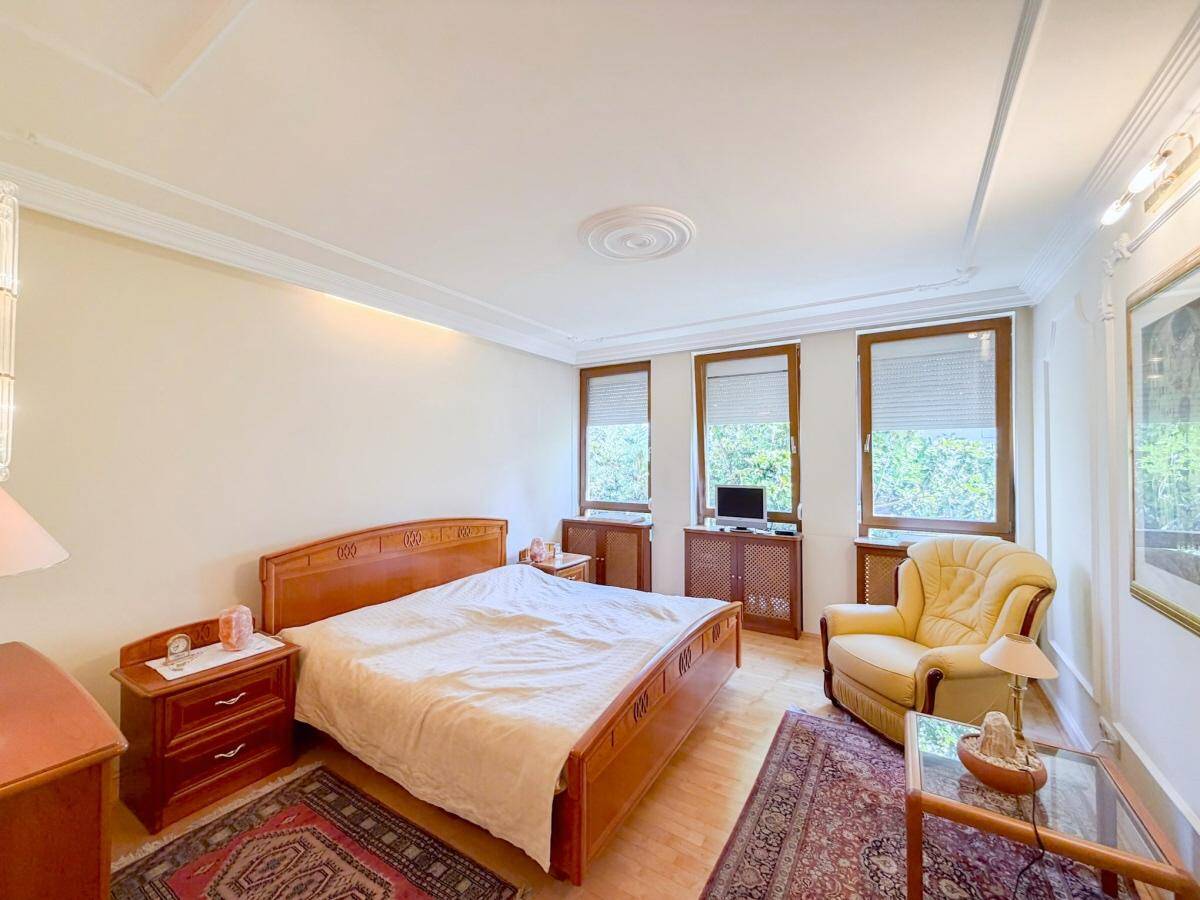 Geräumiges Schlafzimmer mit Doppelbett, Holzmöbeln und drei Fenstern für viel Tageslicht.
