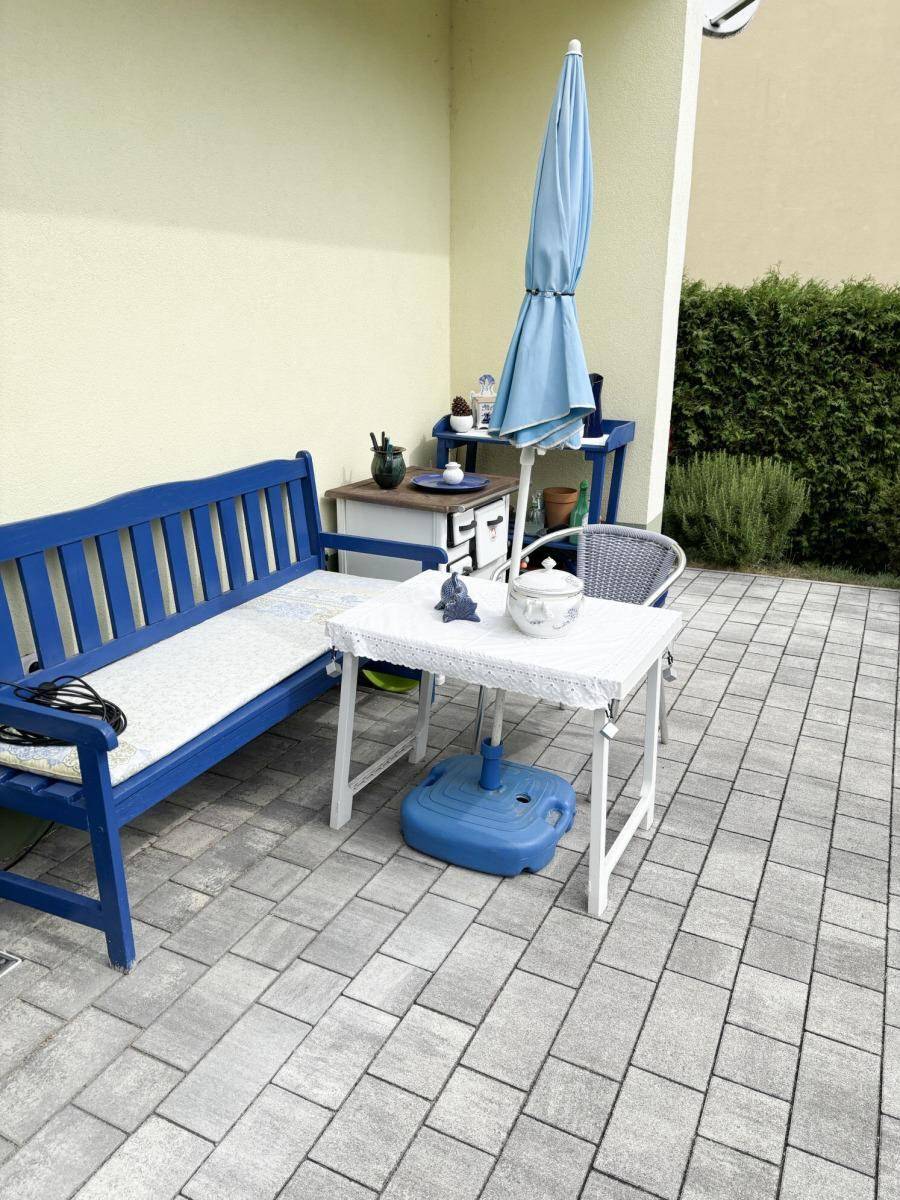 Gemütliche Terrassenecke mit blauer Sitzbank, kleinem Tisch und Sonnenschirm für entspannte Stunden.