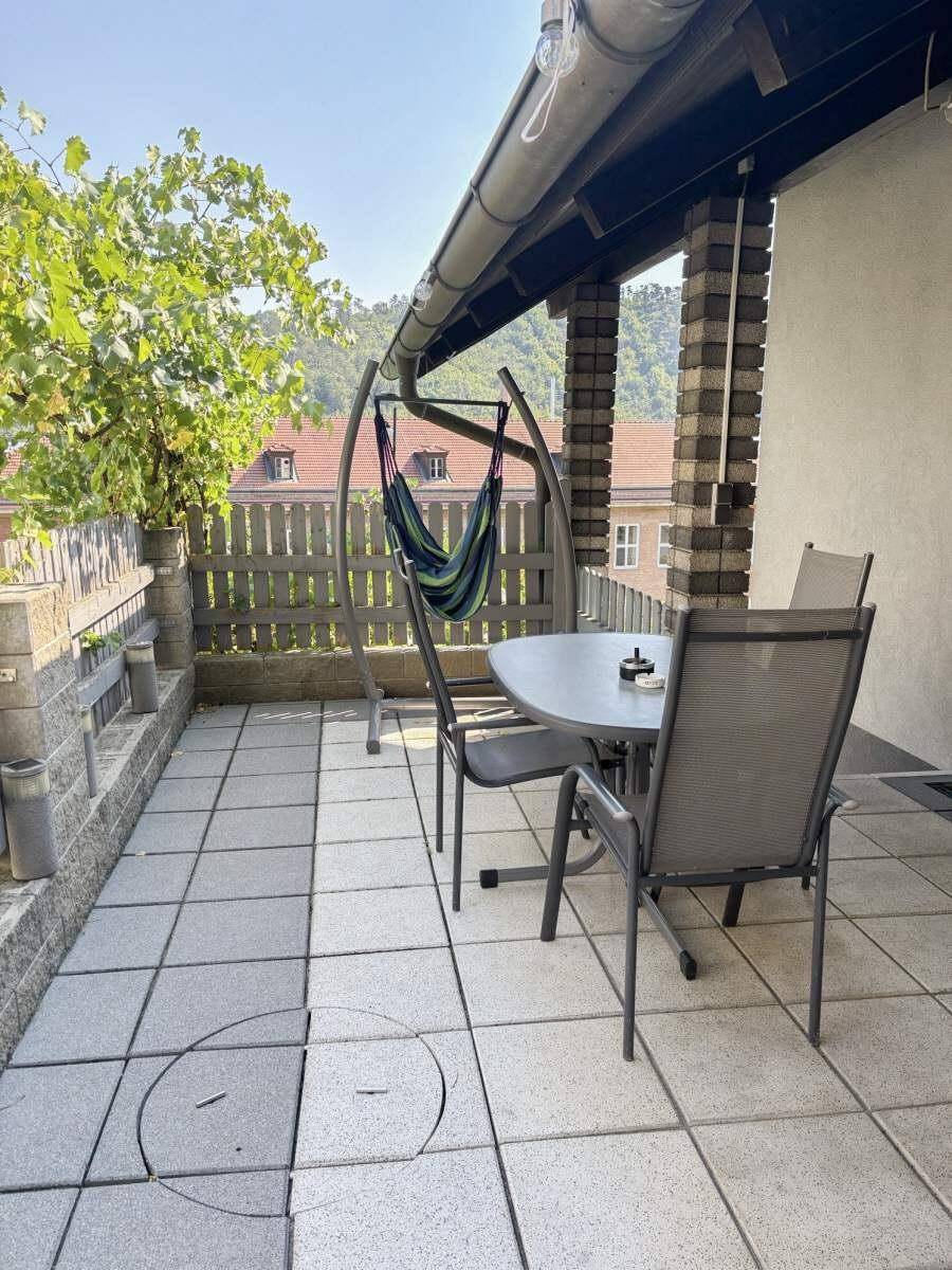 Gepflasterte Terrasse mit Gartenmöbeln und Hängesessel, umgeben von einer Mauer.