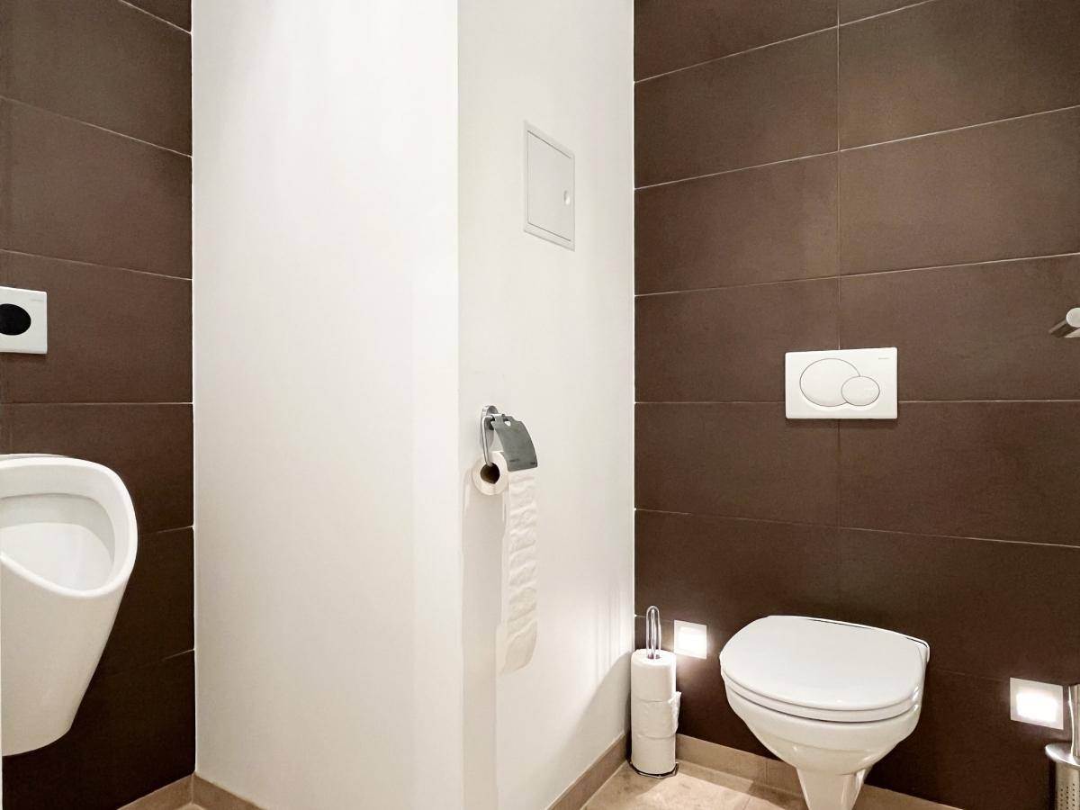 Moderne Gästetoilette mit braunen Fliesen, Urinal und wandhängendem WC, sehr gepflegt und stilvoll.