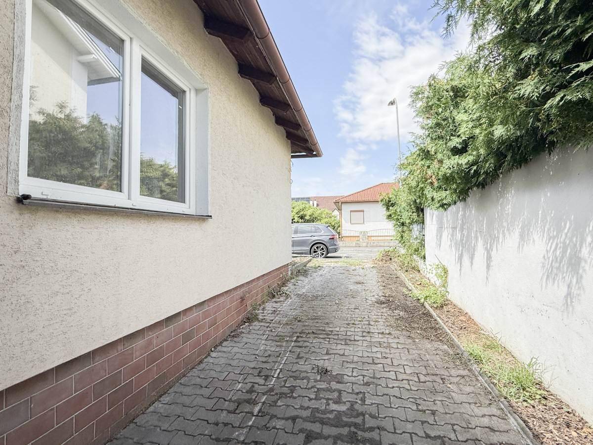 Seitenansicht des Hauses mit gepflasterter Zufahrt und grüner Hecke.
