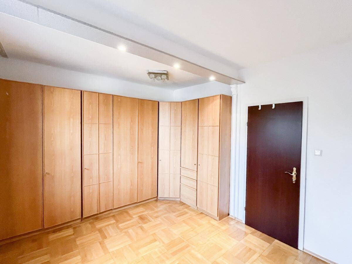Schlafzimmer mit hellem Parkettboden und raumhohen Einbauschränken aus Holz.