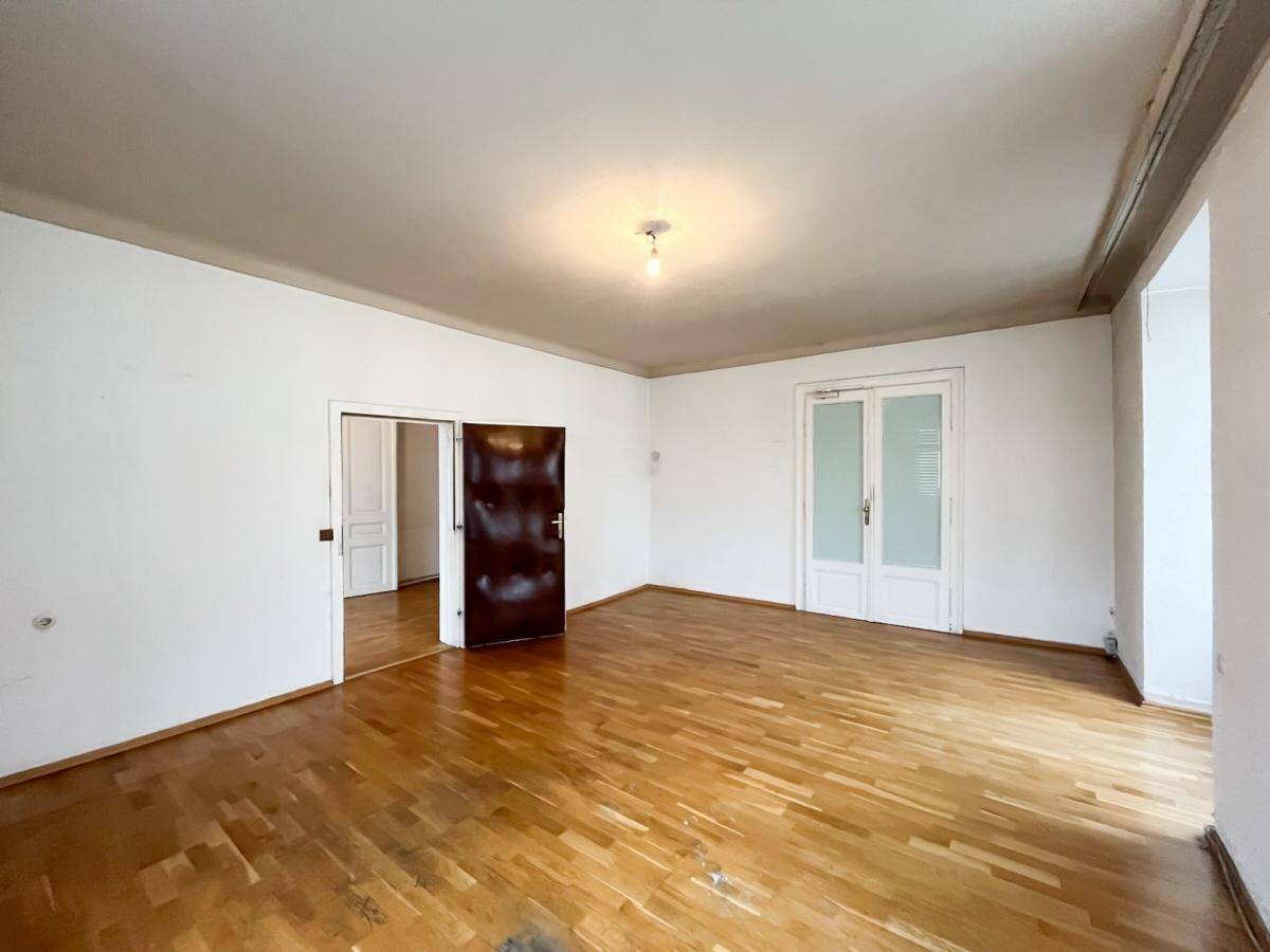 Heller Raum mit Holzboden, weißen Wänden und einer dunklen Holztür, die zu einem anderen Bereich führt.