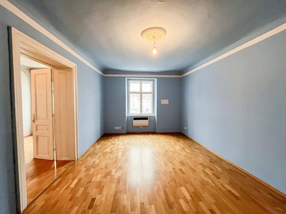 Großes Zimmer mit hellblauen Wänden, Holzboden und einem Fenster, das den Raum mit natürlichem Licht erfüllt.