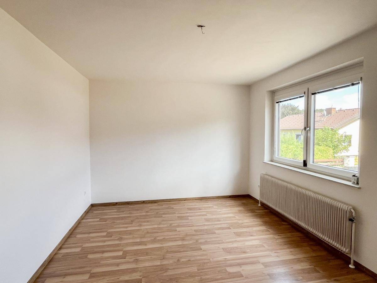 Schlafzimmer mit Laminatboden und Fenster, das viel natürliches Licht hereinlässt.