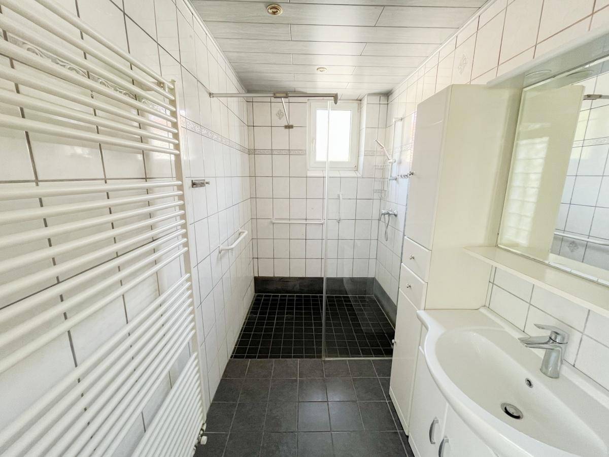 Modernes Badezimmer mit weißen Fliesen, großer begehbarer Dusche und beheiztem Handtuchhalter.