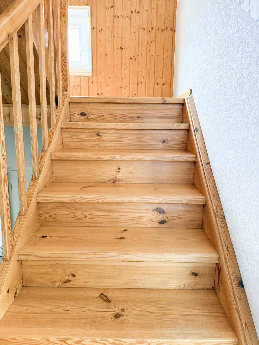 Helle Holztreppe mit Geländer, die in das obere Stockwerk führt, mit Fenster für Tageslicht.