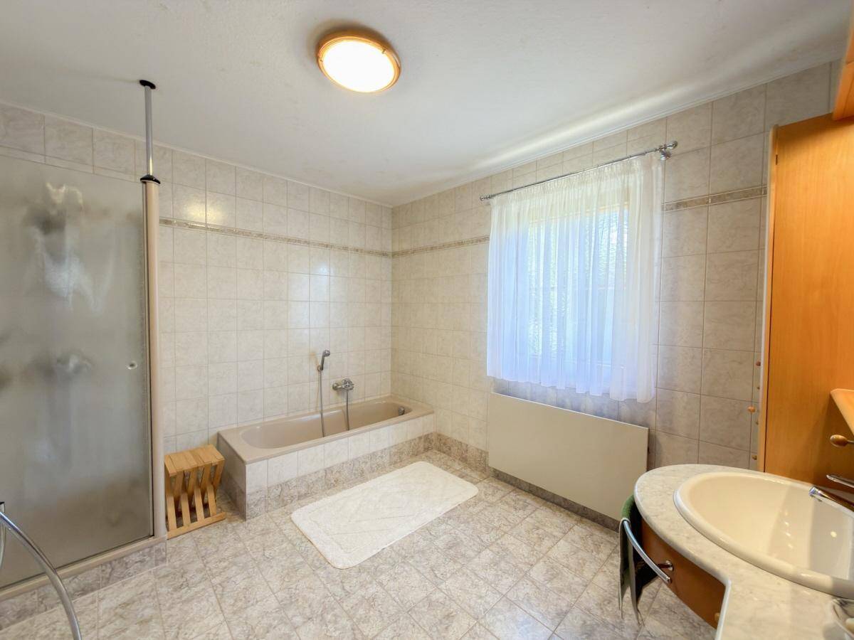Badezimmer mit Badewanne, Dusche, Waschbecken und Fenster.