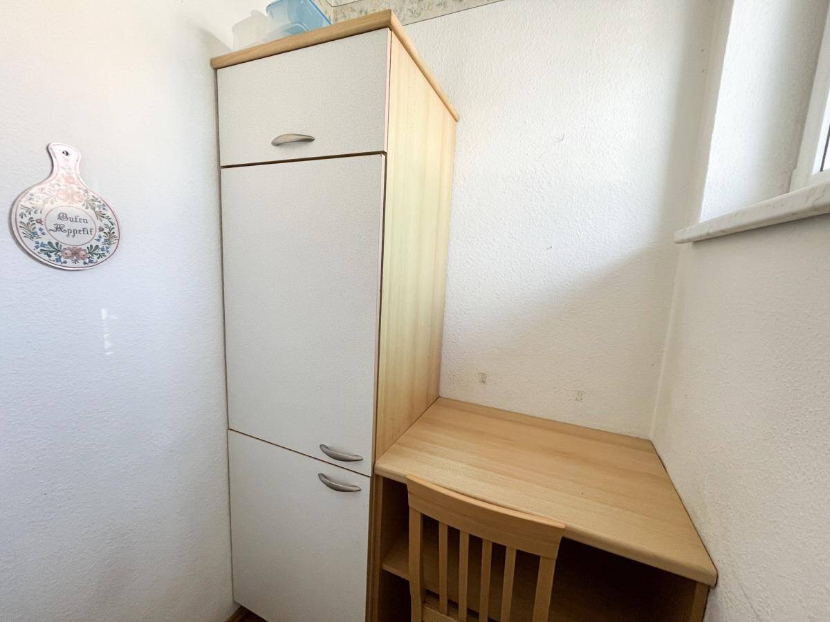 Kleiner Abstellraum mit weißem Hochschrank und einer kleinen Holzarbeitsfläche unter dem Fenster.