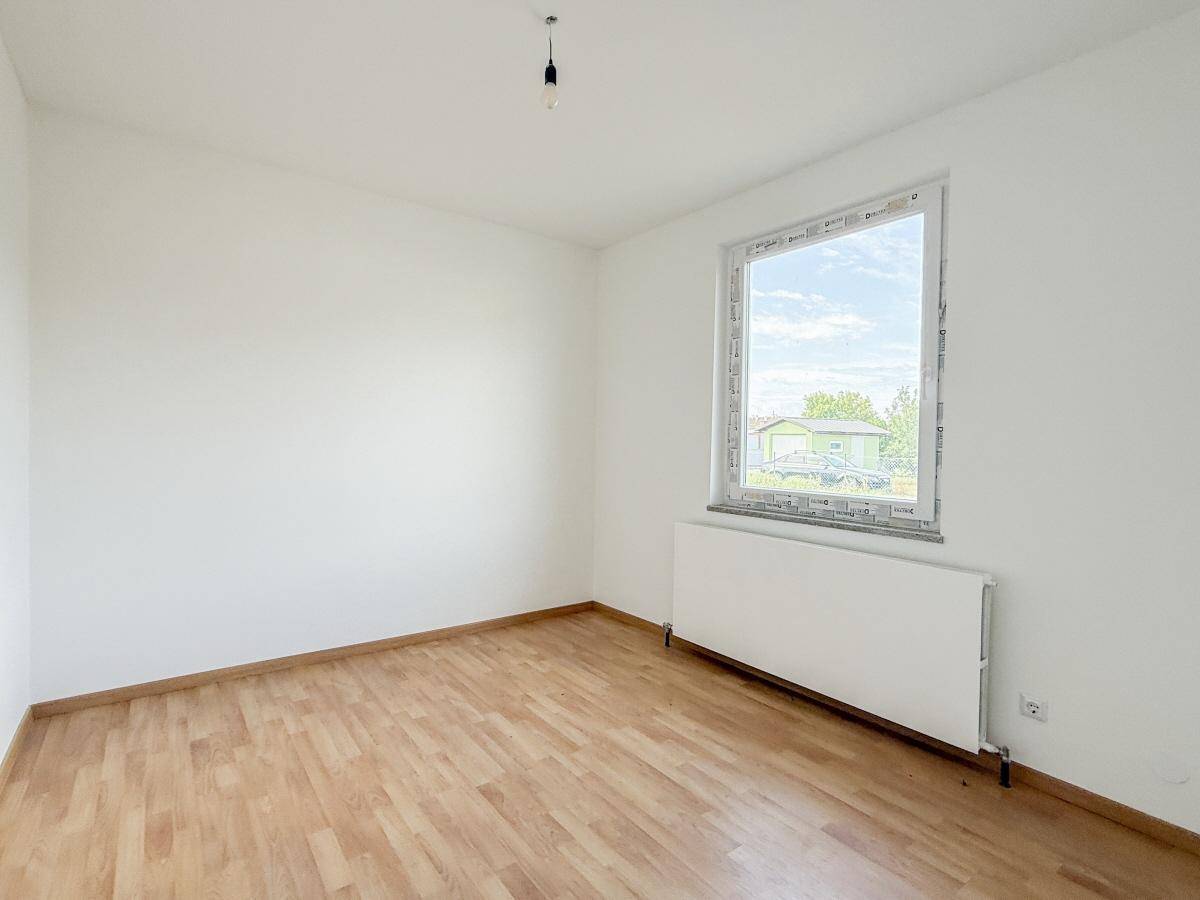 Helles, leeres Zimmer mit Laminatboden und großem Fenster, bereit zur individuellen Gestaltung.