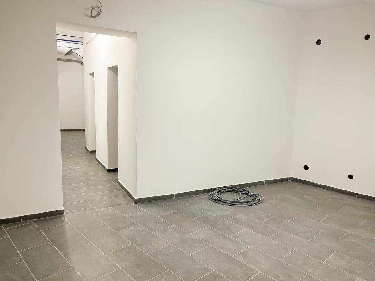 Heller Flur mit grauen Fliesen und weißen Wänden, der zu weiteren Räumen führt.