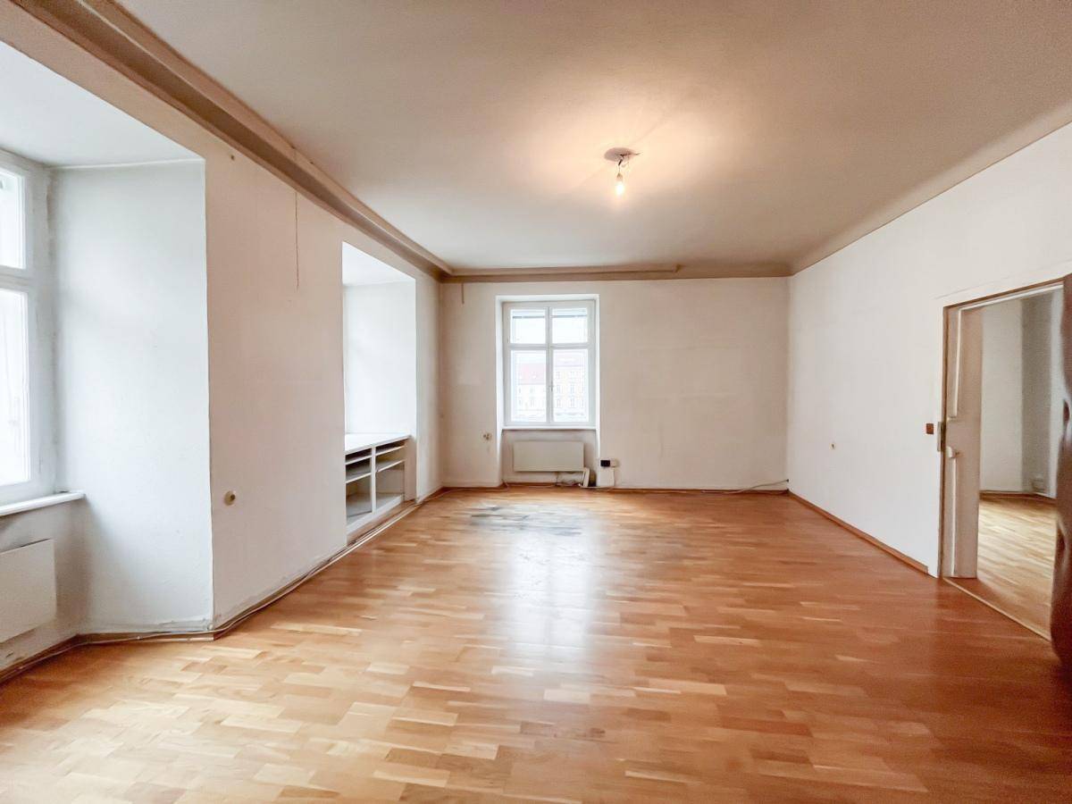 Geräumiges Zimmer mit Holzboden, weißen Wänden, einem Fenster und einer Nische mit integrierten Regalen.