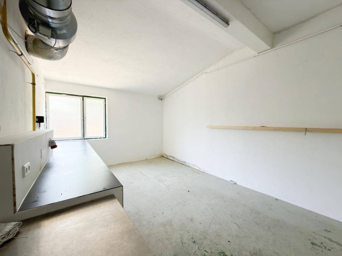 Leerer Nutzraum mit Betonboden, weißen Wänden und einem Fenster, ideal als Lagerfläche.