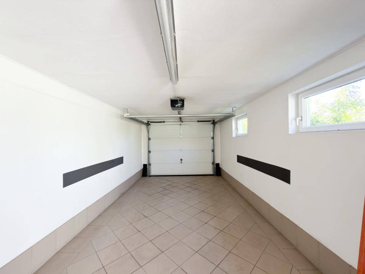 Geräumige Garage mit Fliesenboden, automatischem Tor und Fenstern.