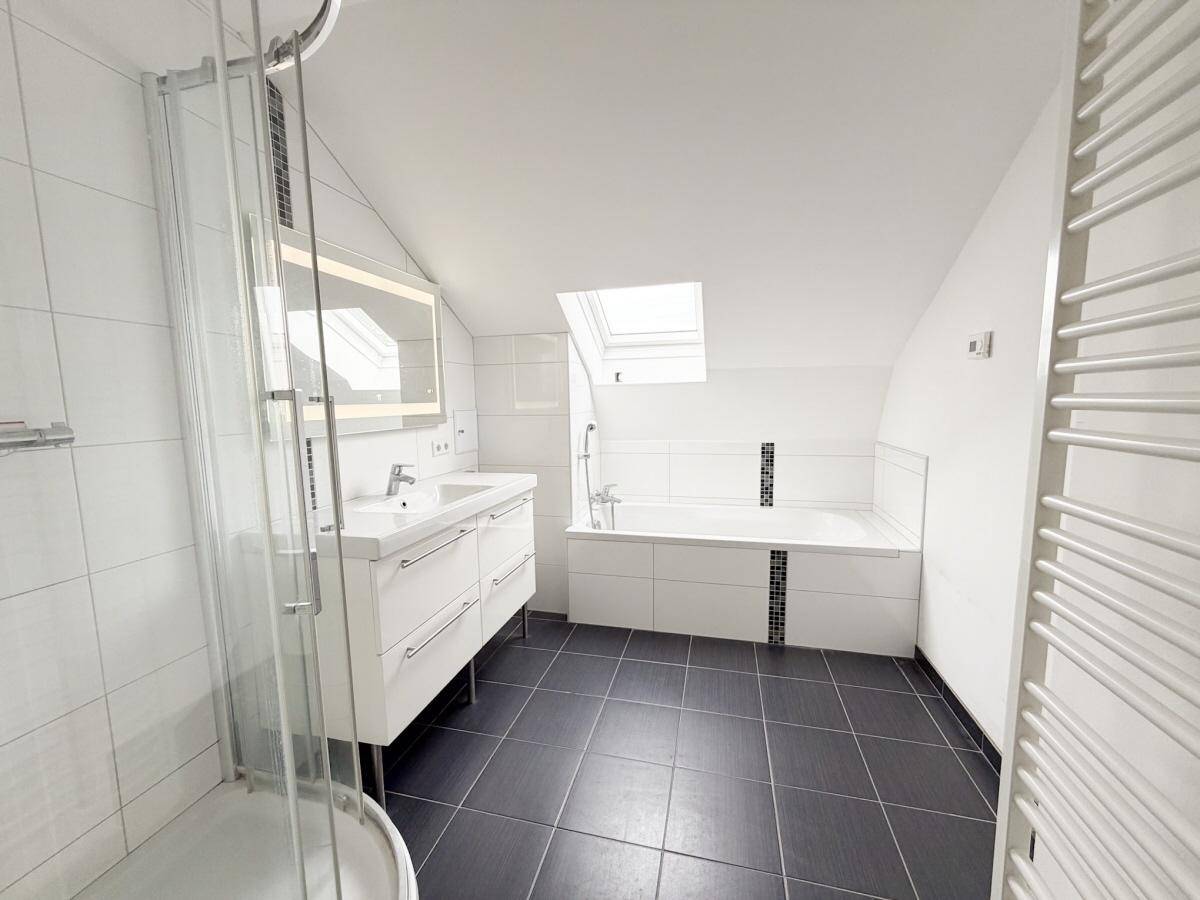 Modernes Badezimmer mit Dusche, Badewanne und Dachfenster für natürliches Licht.