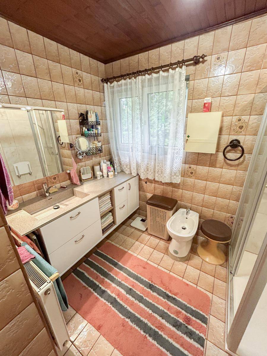 Gefliestes Badezimmer mit Dusche, Waschbecken, Bidet und Holzdecke.