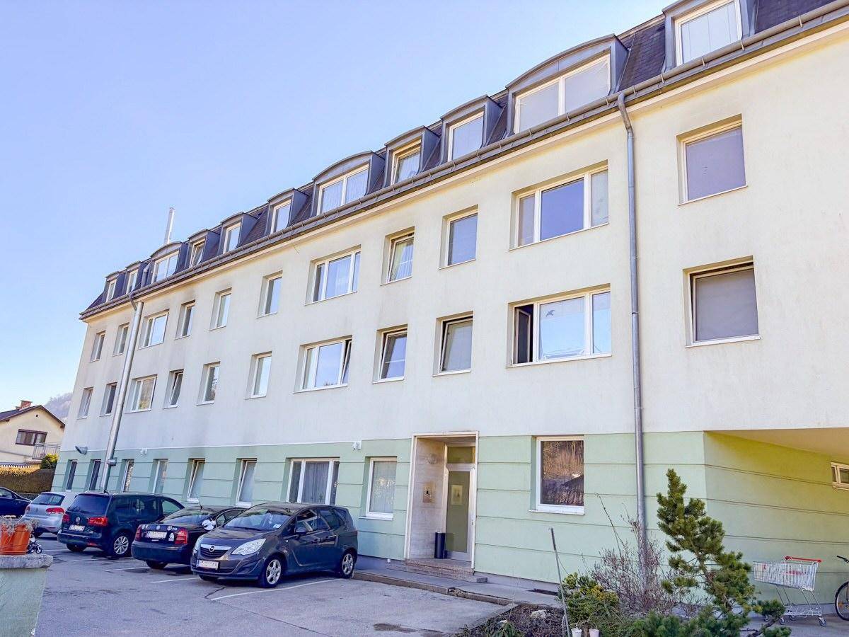 Ansicht der Gebäudefassade mit vielen Fenstern und dem Eingangsbereich sowie geparkten Autos.