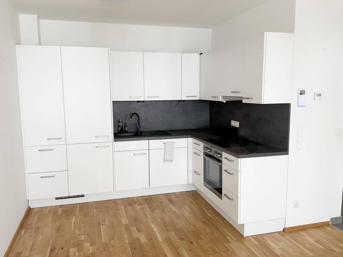 Moderne Einbauküche in Weiß mit dunkler Arbeitsplatte und Holzfußboden.