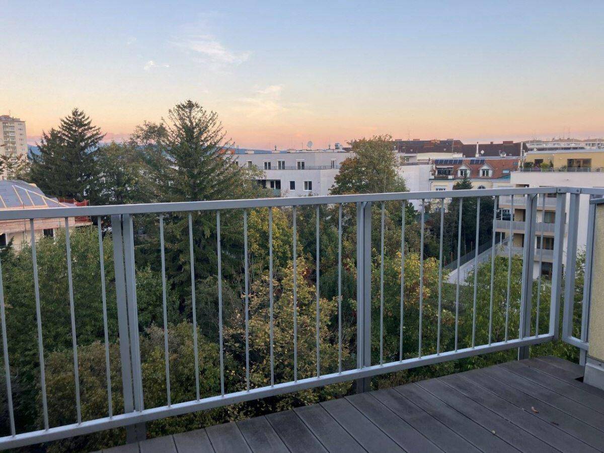 Balkon mit Holzdielen und Metallgeländer bei Sonnenuntergang, bietet einen weiten Blick über die Stadt.