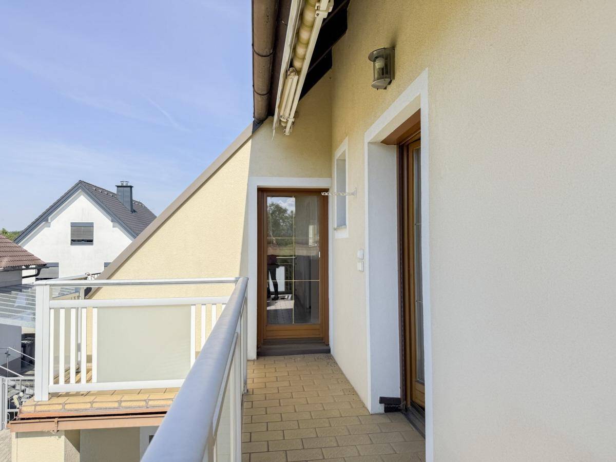 Schmaler Balkon mit Fliesenboden und Blick auf die umliegende Wohngegend und Natur.