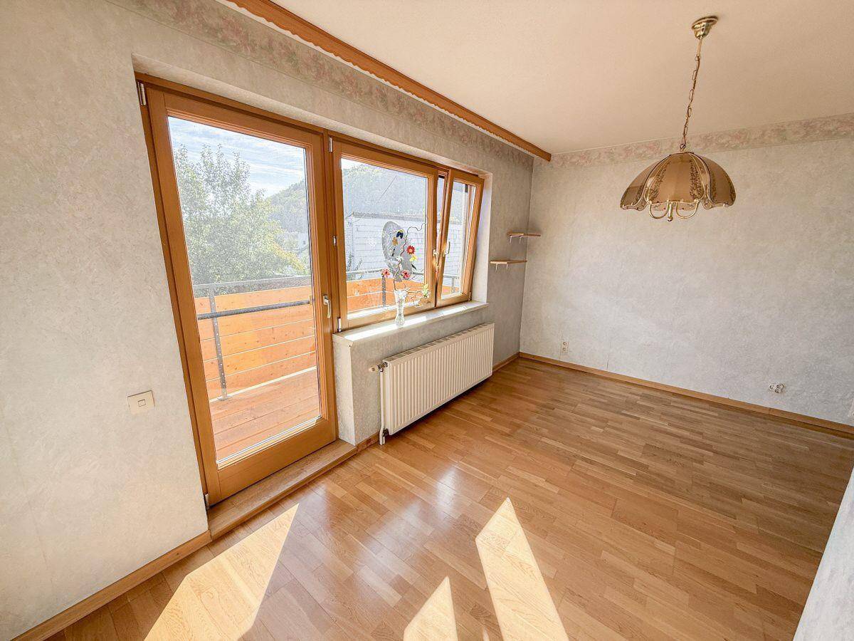Helles Schlafzimmer mit Parkettboden und Zugang zu einem Balkon, bietet viel Tageslicht.