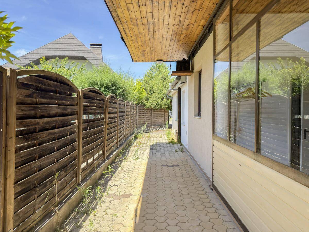 Gepflasterter Weg entlang des Gebäudes mit einem hohen Holzzaun.