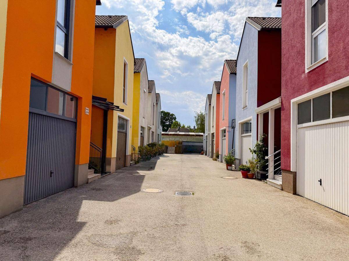 Reihenhauszeile mit farbenfrohen Fassaden und Garagen entlang einer ruhigen Zufahrtsstraße.