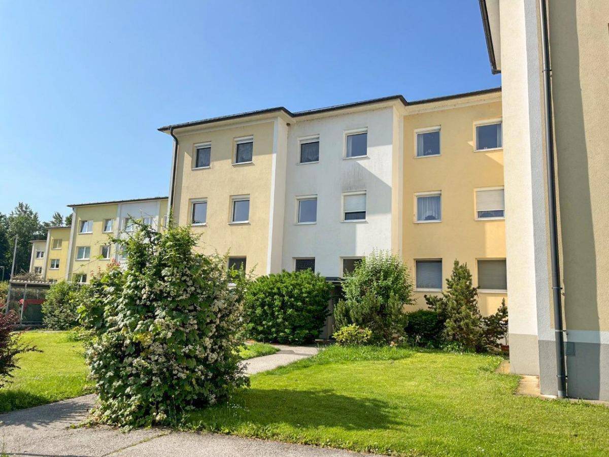 Mehrfamilienhaus mit gelb-weißer Fassade und gepflegter Grünfläche im Vordergrund.