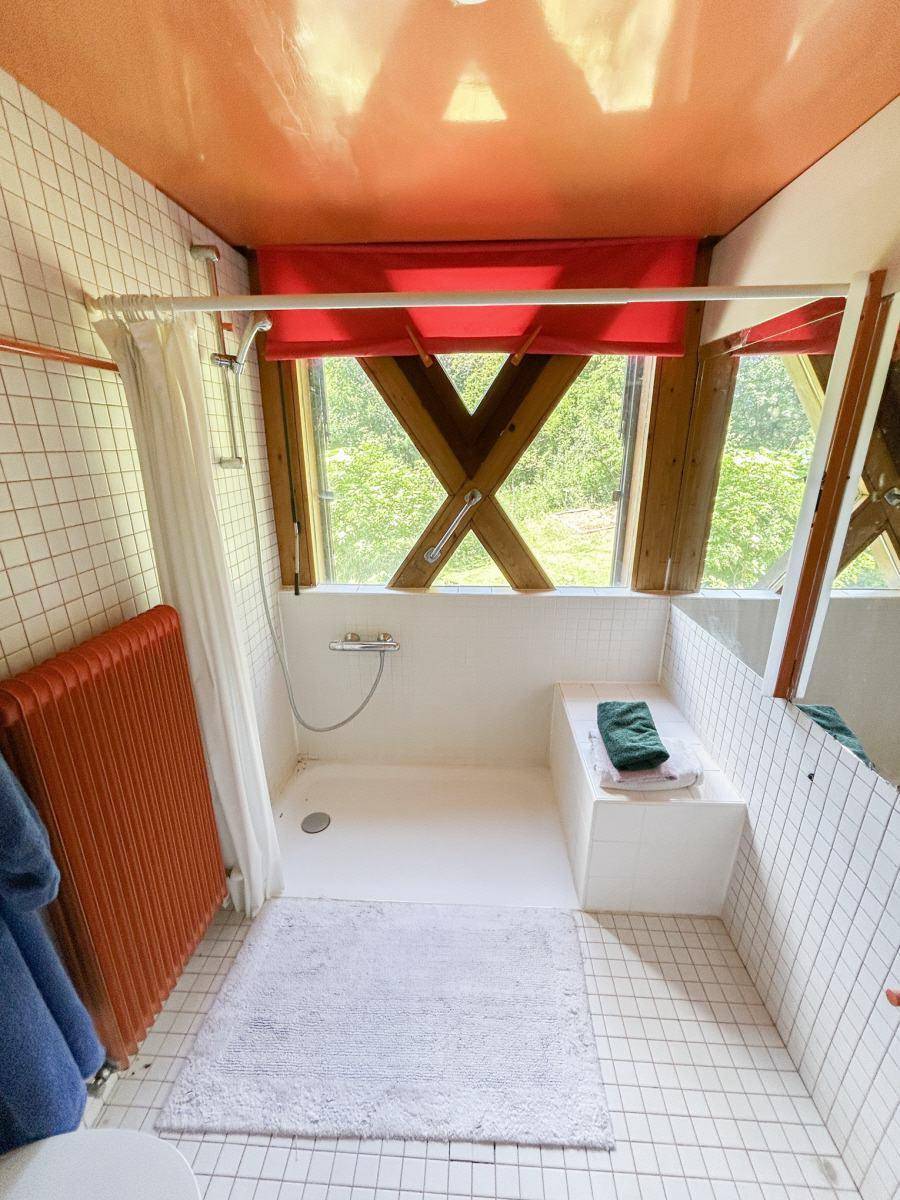 Helles Badezimmer mit Duschbereich, Fenster und orangefarbenem Heizkörper.