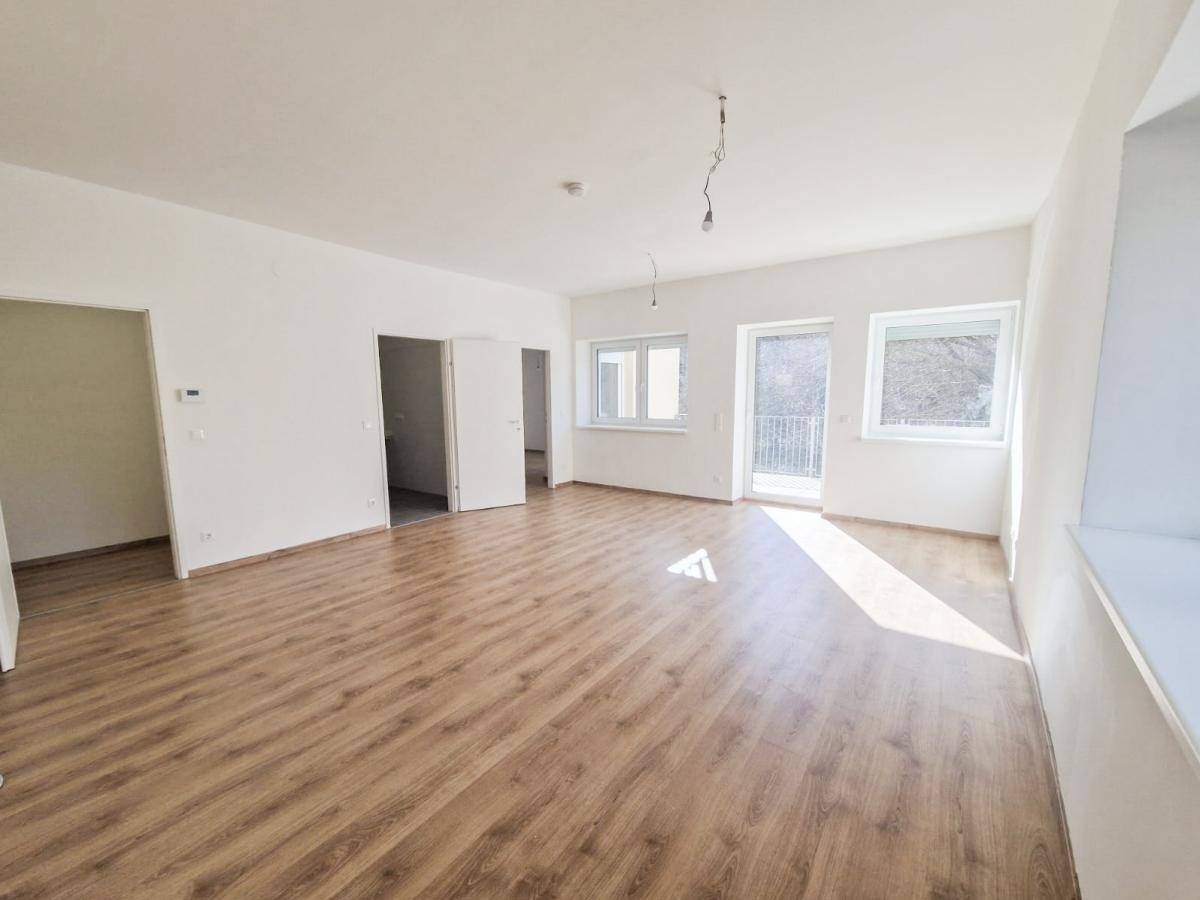 Heller, unmöblierter Wohnbereich mit Laminatboden und Zugang zu einem kleinen Balkon.