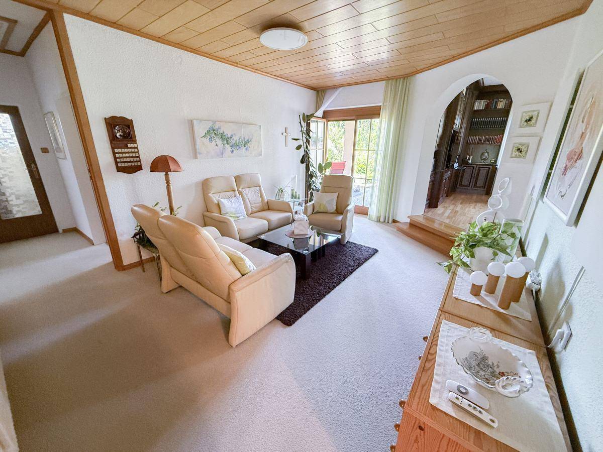 Gemütliches Wohnzimmer mit Teppichboden, Holzdecke und Zugang zu einem weiteren Raum.