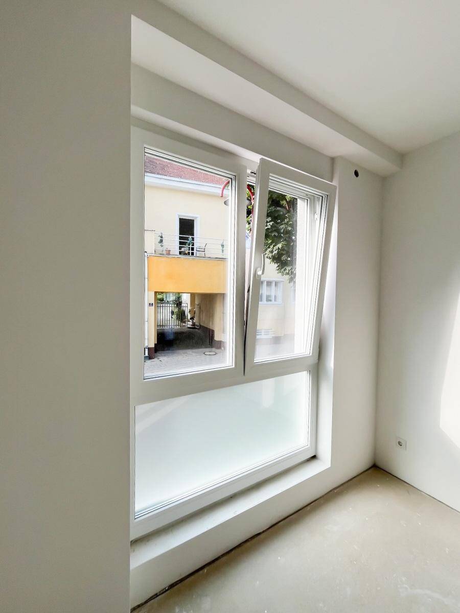 Geöffnetes Fenster mit Blick auf einen Innenhof und ein gegenüberliegendes Gebäude.