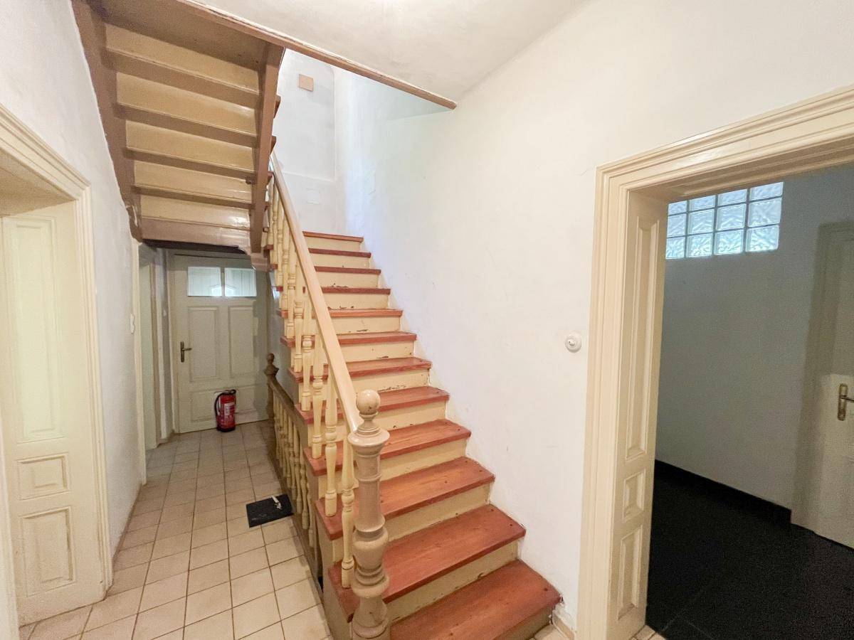 Treppenhaus mit Holztreppe, Fliesenboden und traditionellem Geländer.
