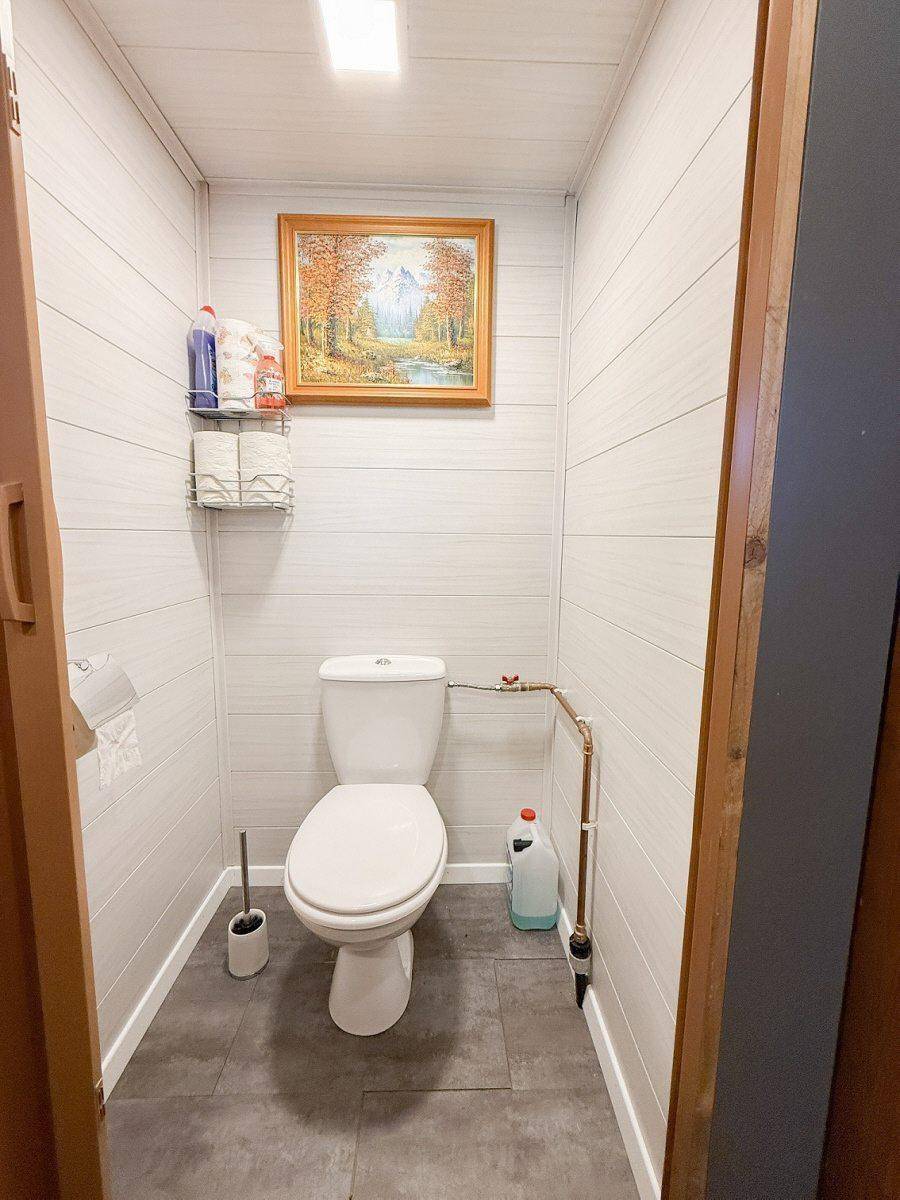 Kleines WC mit weißen Holzpaneelen, dunklem Fliesenboden und einem Fenster für Tageslicht.