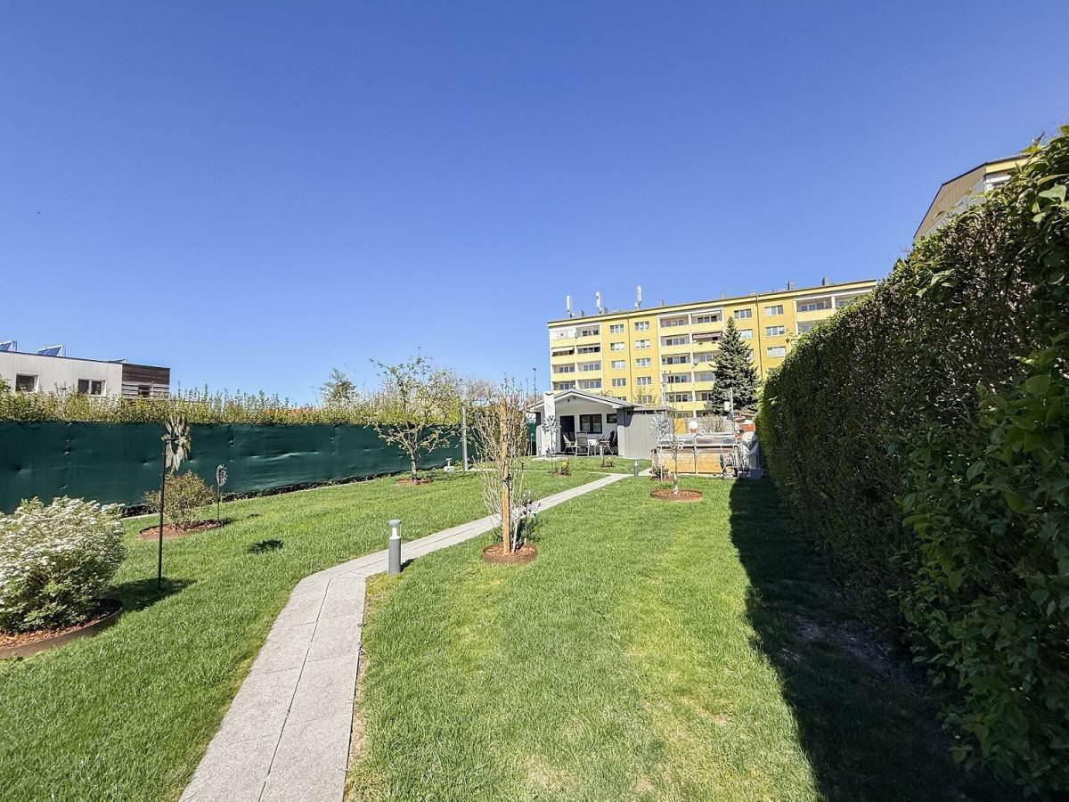 Weitläufiger Garten mit Rasenfläche, umgeben von Hecken und Blick auf umliegende Gebäude.