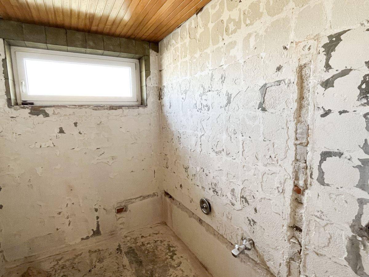 Badezimmer im Rohzustand mit Fenster, bereit für eine Renovierung.