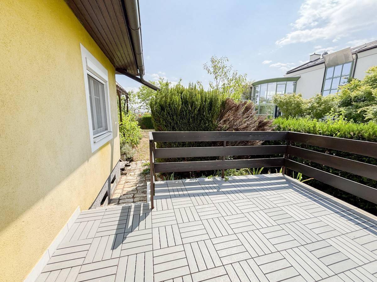 Kleine, geflieste Terrasse mit Holzzaun und Blick auf die grüne Umgebung.