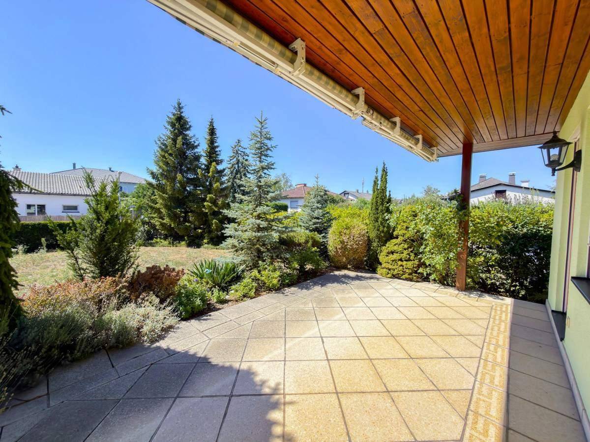 Überdachte Terrasse mit Fliesenboden und Blick in den Garten.