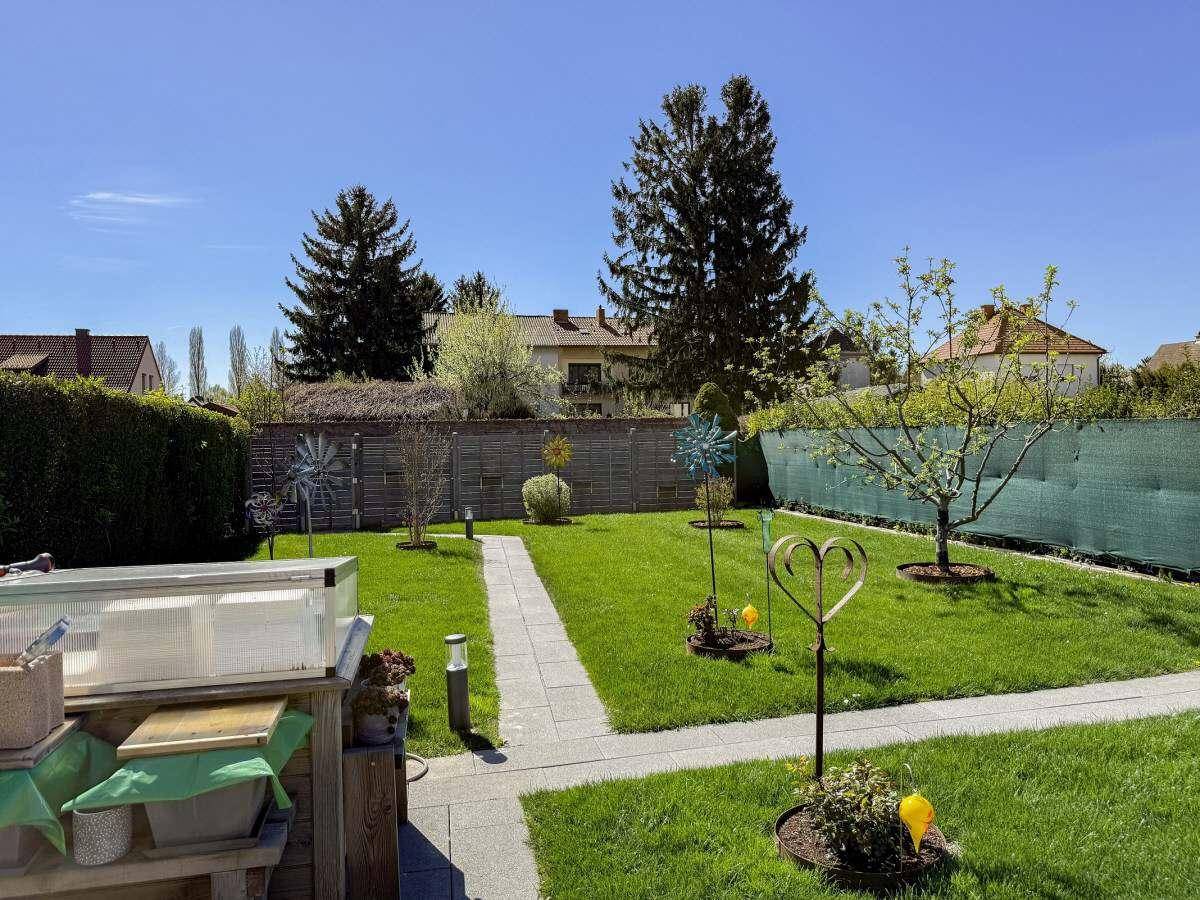 Sonniger Garten mit gepflegtem Rasen, Steinweg und einem kleinen Hochbeet für Pflanzen.