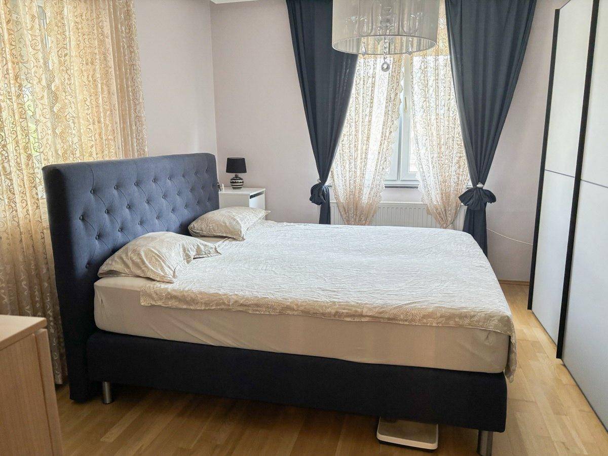 Gemütliches Schlafzimmer mit großem Doppelbett, Holzboden und Vorhängen an den Fenstern.