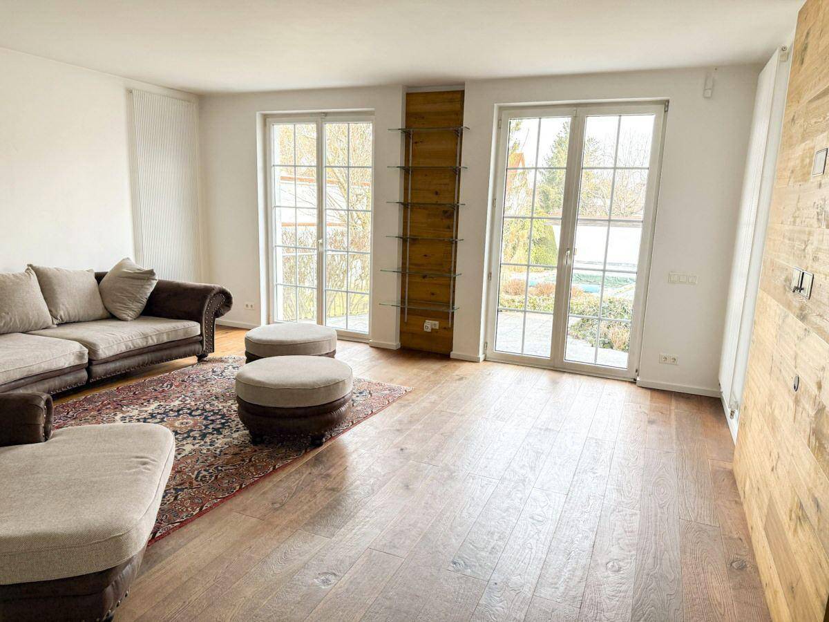 Helles Wohnzimmer mit Holzdielenboden, großen Fenstern und direktem Zugang zum grünen Garten.