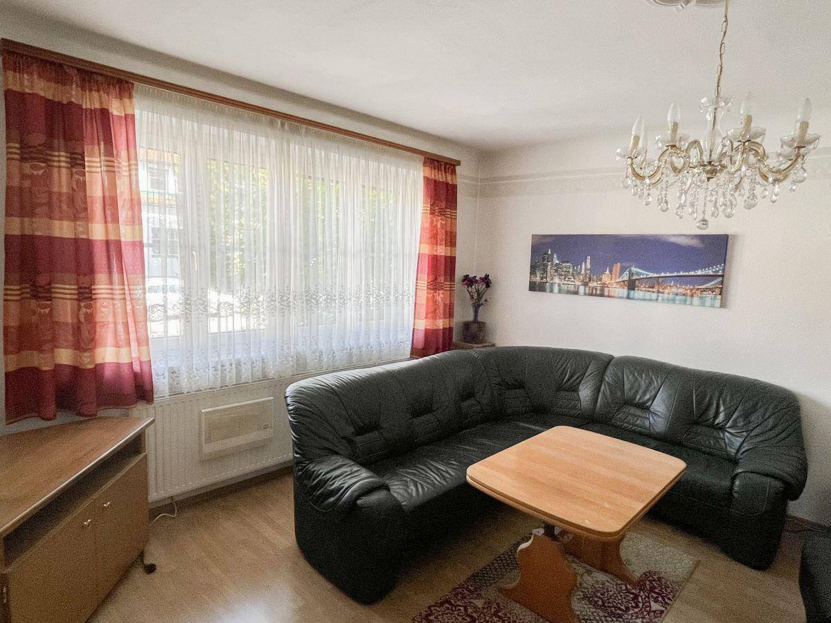 Wohnzimmer mit dunklem Ledersofa, Holztisch und großem Fenster, beleuchtet von einem Kronleuchter.